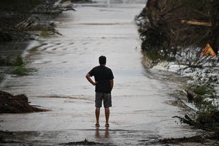 A man looks at a damaged road after severe flash flooding that occurred during the July 4 holiday weekend, in Hunt, Texas, on July 6, 2025. Rescuers in Texas raced against time Sunday to find dozens of missing people, including children, swept away by flash floods that killed at least 59, as forecasters warned of new deluges. Local Texans joined forces with disaster officials to search through the night for the missing, including 27 girls from a riverside Christian summer camp. Texas Governor Greg Abbott said Camp Mystic on the banks of the Guadalupe River, where some 750 girls had been staying when the floodwaters hit, had been